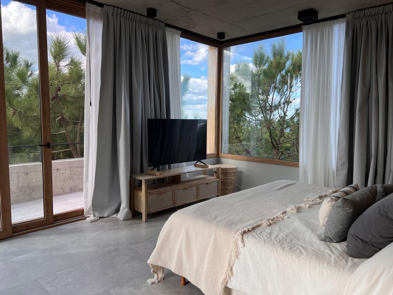 Suite con cortinados de tela gris y sheer en ventanales esquina con vista a pinos